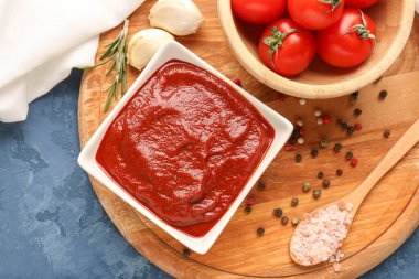 Bir kase lezzetli domates ezmesi, sarımsaklı karanfil ve mavi grunge arka planda biber.