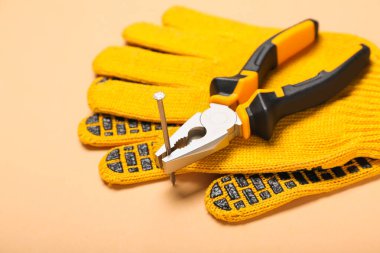 Bej arka planda tırnak ve eldivenli pense.