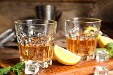 Ahşap zemin üzerinde rom, limon ve buz küpleri olan tahta, yakın plan.