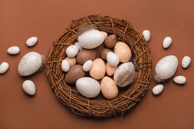 Kahverengi arka planda Paskalya yumurtaları ve tüyleriyle çelenk