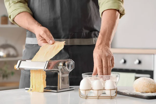 Man making pasta with machine at table in kitchen, closeup