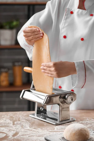 Female chef making pasta with machine at table in kitchen, closeup