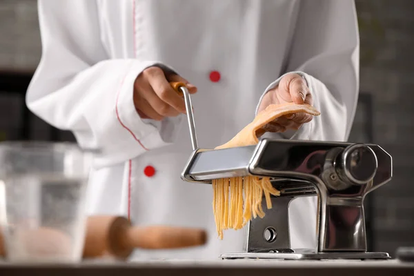 Female chef making pasta with machine at table in kitchen, closeup