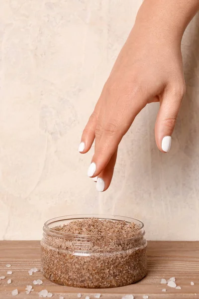Female hand with jar of body scrub on wooden table, closeup