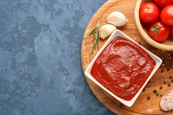 Schüssel Mit Leckerer Tomatenmark Knoblauchzehen Und Pfefferkorn Auf Blauem Grunge — Stockfoto