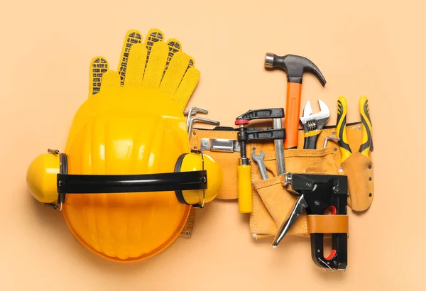 Hardhat, hearing protectors and pliers in belt with tools on beige background
