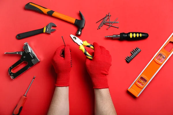 男性手戴手套 手持钳子和钉子 靠近不同的红色背景工具 — 图库照片