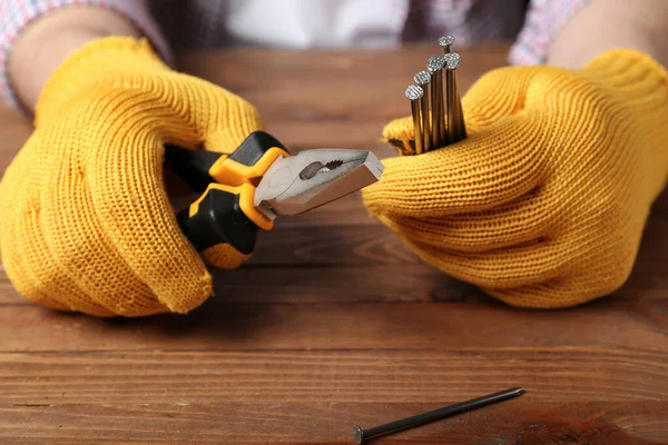 Male hands in gloves holding pliers and nails on wooden background