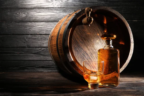 濃い木製の背景にガラスとおいしいウイスキーのボトルとオーク樽 — ストック写真
