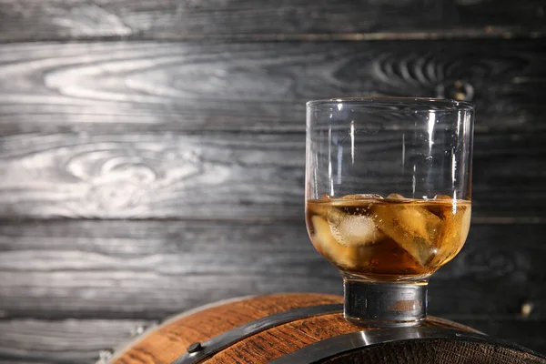 stock image Glass of cold whiskey on barrel against dark wooden background