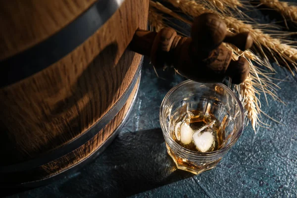 Barrel with glass of cold whiskey on dark background