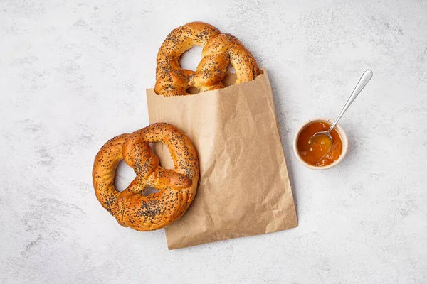 Paper bag with tasty pretzels and jam on light background