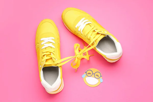 Sneakers with tied shoe laces and paper smile on pink background. April Fools\' Day celebration
