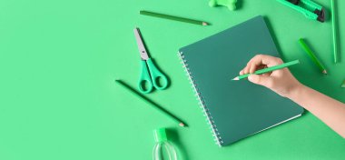 Yeşil zemin üzerinde defter ve kırtasiye malzemesi olan ve metin için alanı olan bir çocuk eli