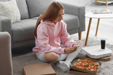 Evde cep telefonu kullanan lezzetli pizzalı genç bir kadın.