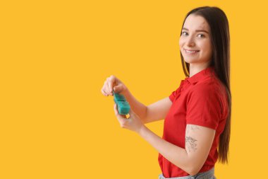 Young woman with container of vitamin supplements on yellow background