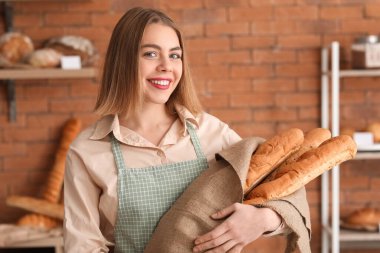 Female baker with fresh baguettes in kitchen