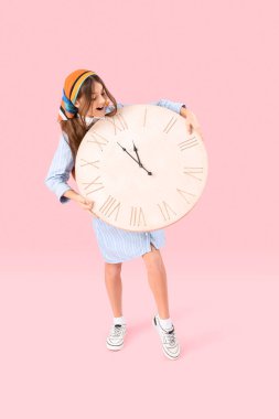 Pembe arka planda büyük duvar saati olan küçük kız.