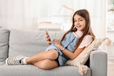 Kol saati ve tablet bilgisayarı olan küçük kız evdeki kanepede yatıyor.