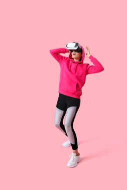 Pretty young woman in VR glasses on pink background