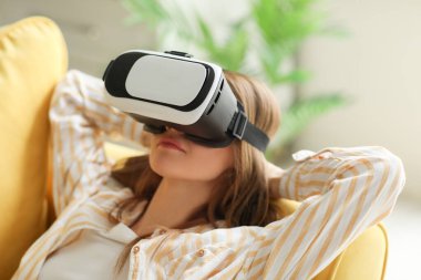 Pretty young woman in VR glasses lying in sofa at home
