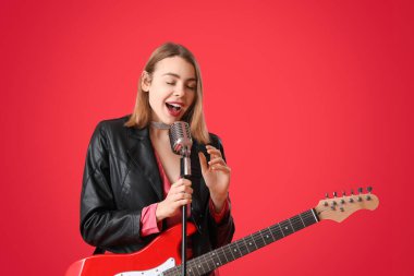 Kırmızı arka planda gitar ve mikrofonlu genç bir kadın şarkı söylüyor.