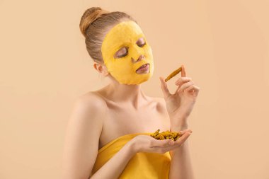 Young woman with turmeric sheet mask and roots on beige background, closeup