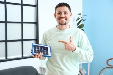 Yakışıklı adam odadaki taşınabilir güneş panelini işaret ediyor.