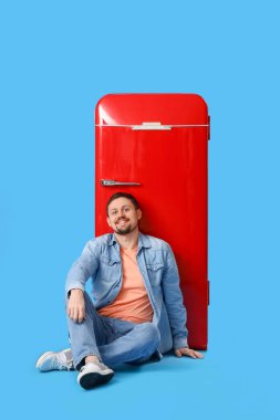 Büyük boş posterli yakışıklı adam mavi arka planda oturuyor.