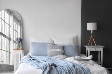 Ayna ve vazoda bahar çiçekleriyle aydınlık yatak odasının içinde.