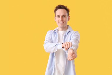 Genç adam sarı arka planda kolunu kıvırıyor.