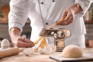 Erkek aşçı mutfaktaki masada makineli makarna yapıyor, yakın plan.