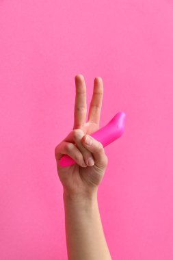 Süpürge vibratörlü kadın pembe arka planda zafer işareti gösteriyor.