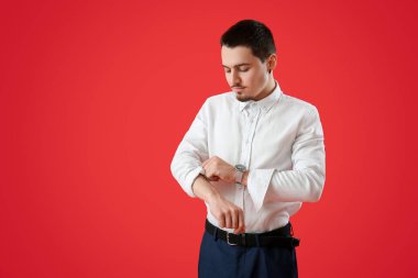 Genç iş adamı kırmızı arka planda kolunu kıvırıyor.