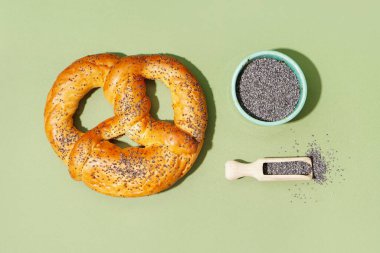 Tasty pretzel and bowl of poppy seeds on color background clipart