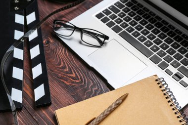 Gözlüklü dizüstü bilgisayar, film alkışı ve koyu ahşap arka planda not defteri, yakın plan.