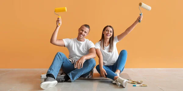 幸福的年轻夫妇与油漆辊坐在地板上在他们的新房子 — 图库照片