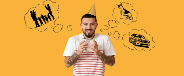 Happy man with birthday gift making wishes on yellow background