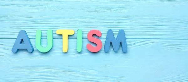 Word AUTISM on light blue wooden background