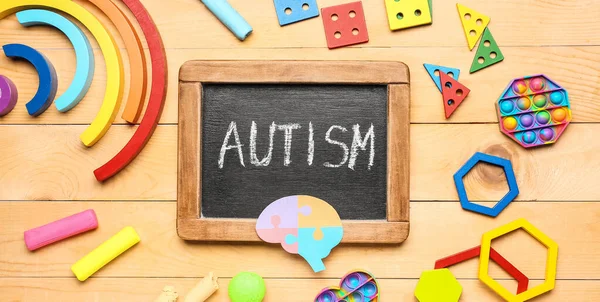 Board with word AUTISM and toys on wooden background