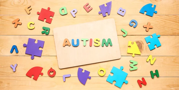 Word AUTISM, letters and puzzle pieces on wooden background