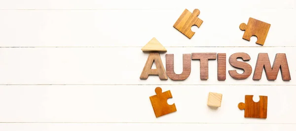 Word AUTISM and puzzle pieces on white wooden background with space for text