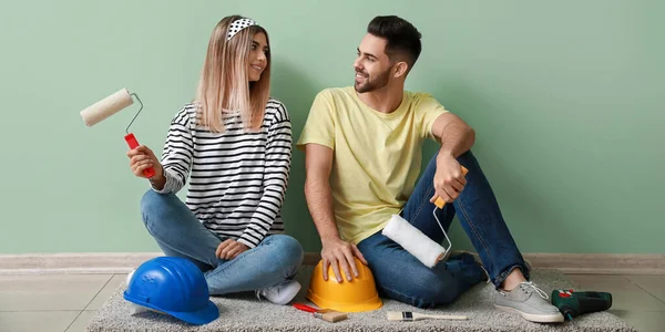 在新房子里 一对快乐的年轻夫妇坐在地板上 手里拿着粉刷和硬帽子 — 图库照片