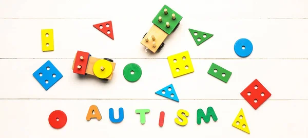 Toys and word AUTISM on white wooden background