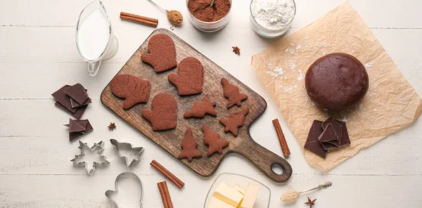 stock image Board with tasty Christmas chocolate cookies, dough and ingredients on white wooden background