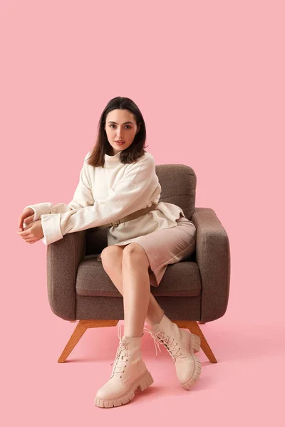 若いです女性座っていますで柔らかいアームチェア上のピンクの背景 — ストック写真
