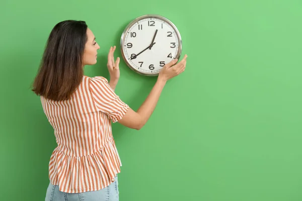Young woman hanging clock on green wall, back view
