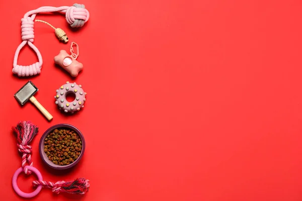 Different pet care accessories and bowl of dry food on red background