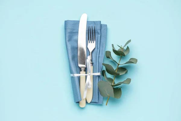 stock image Set of cutlery in napkin and eucalyptus branch on blue background