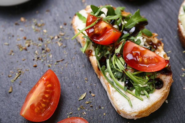 Tasty sandwich with cream cheese, arugula and tomatoes on slate board, closeup